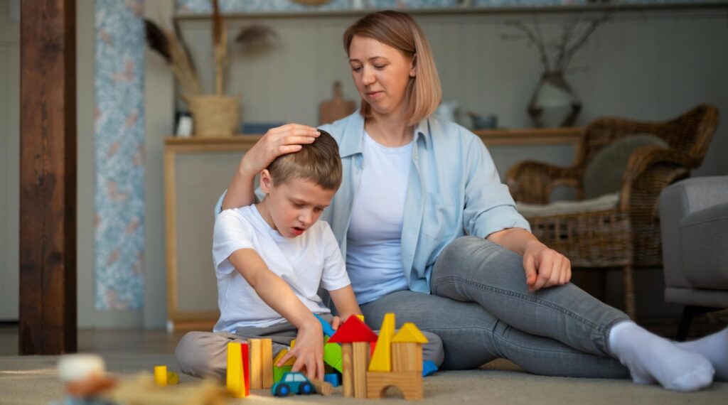 Mother comforts her son as he plays with wooden blocks, offering support and care