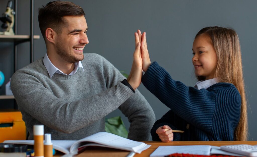 Smiling teacher and young girl high-fiving in a classroom, celebrating a learning moment 