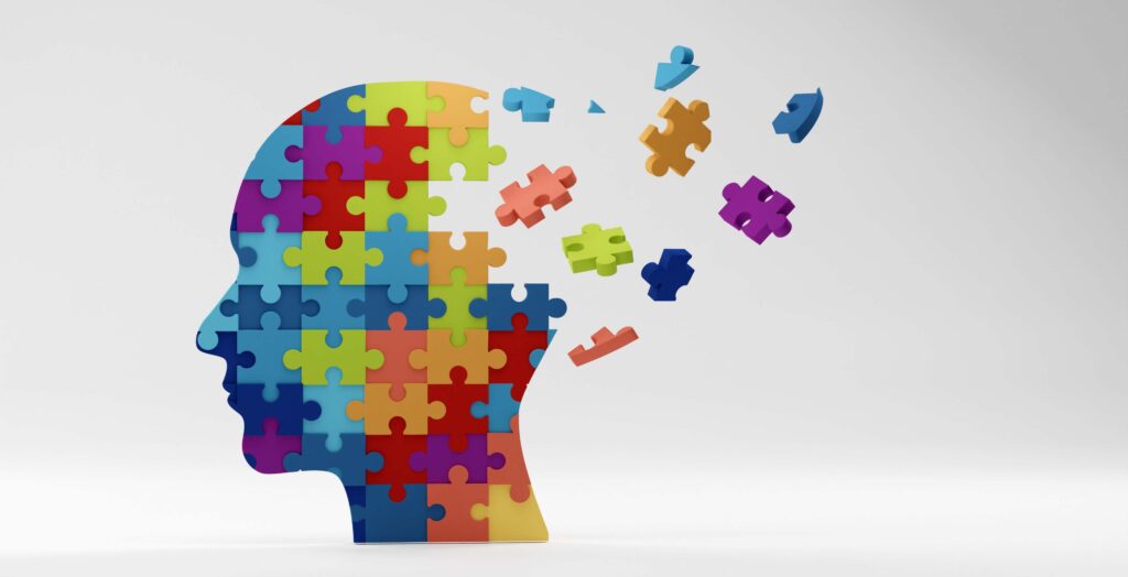 A human head silhouette filled with colorful puzzle pieces, some floating away, against a light gray background.