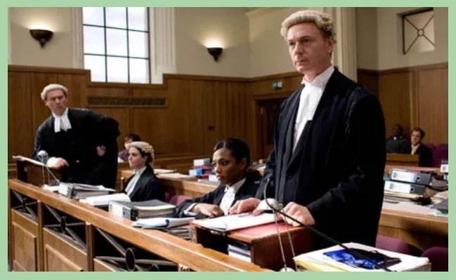 A courtroom scene with barristers in wigs and gowns, one standing to speak, in a panelled room.